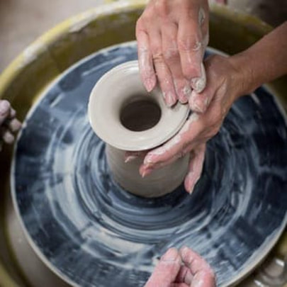 A student's hands throwing a pot on a pottery wheel